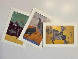 A set of three original art greeting cards from the GC02 Chakor collection arranged on a white surface, showcasing a figurative Mughal-style portrait of a royal man holding a royal woman on a gold background, a floral design on a mint green background, and a fauna-themed bird print on an ochre-gold background.
