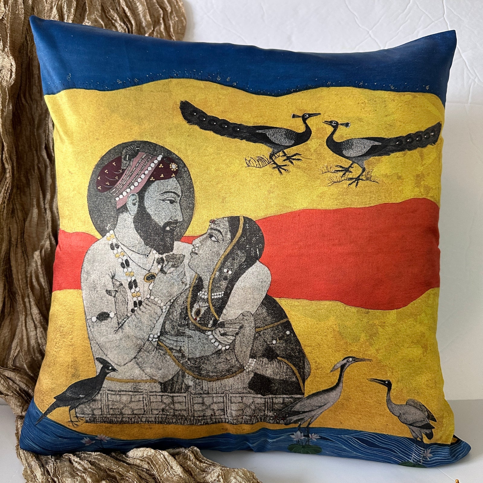 An 18x18 gaze peacock miniature art cushion cover by Sumaira Tazeen featuring a Mughal royal figures with peacocks and herons on a vibrant blue, red, and yellow backdrop.