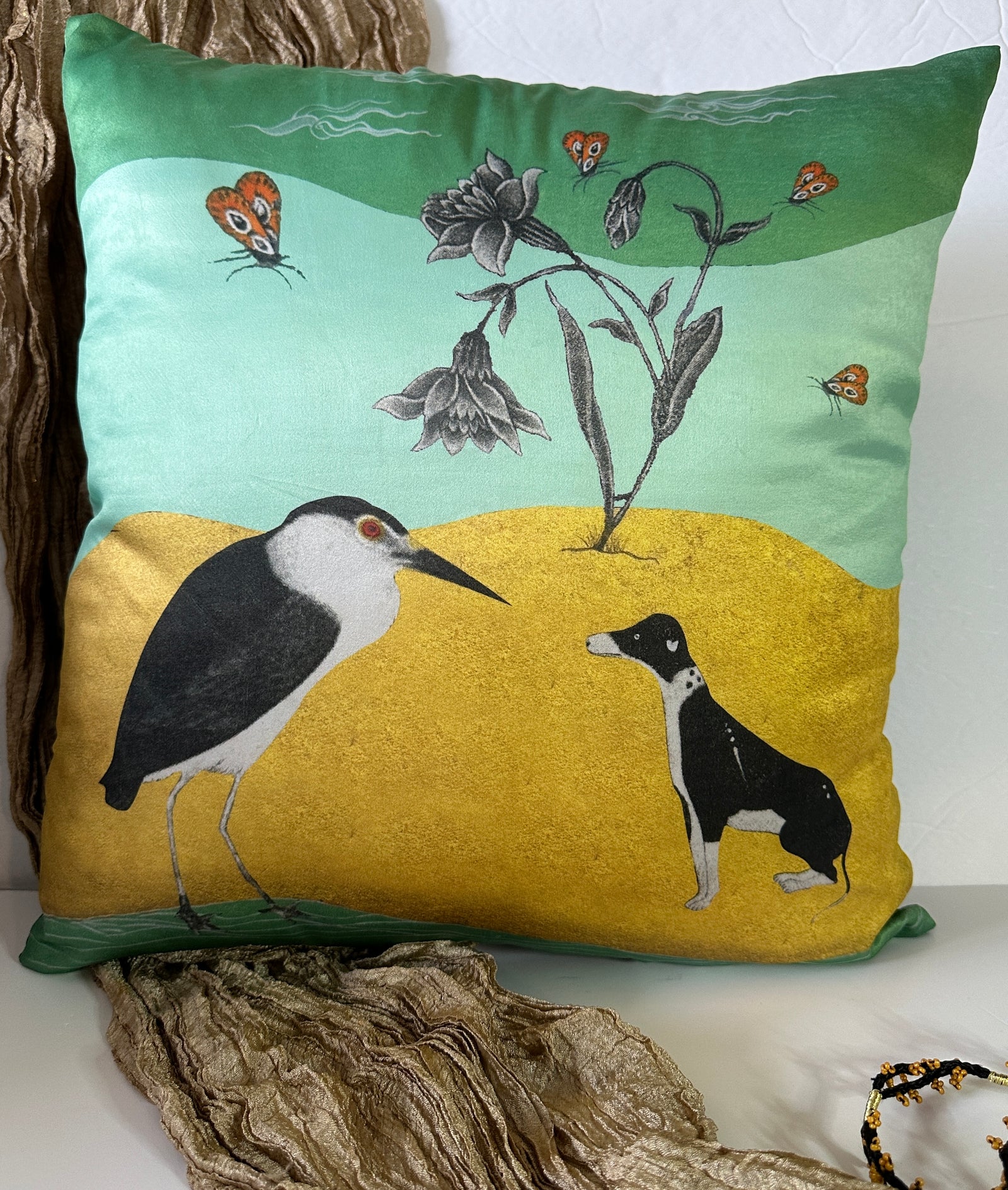 A premium quality polysilk Mughal art cushion cover by Sumaira Tazeen featuring a black and white heron and a dog on a gold-textured ground with a floral background.
