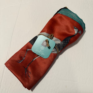 A rolled red poly silk miniature art cushion cover with an artist tag, highlighting the soft sheen and artisan packaging by Sumaira Tazeen.