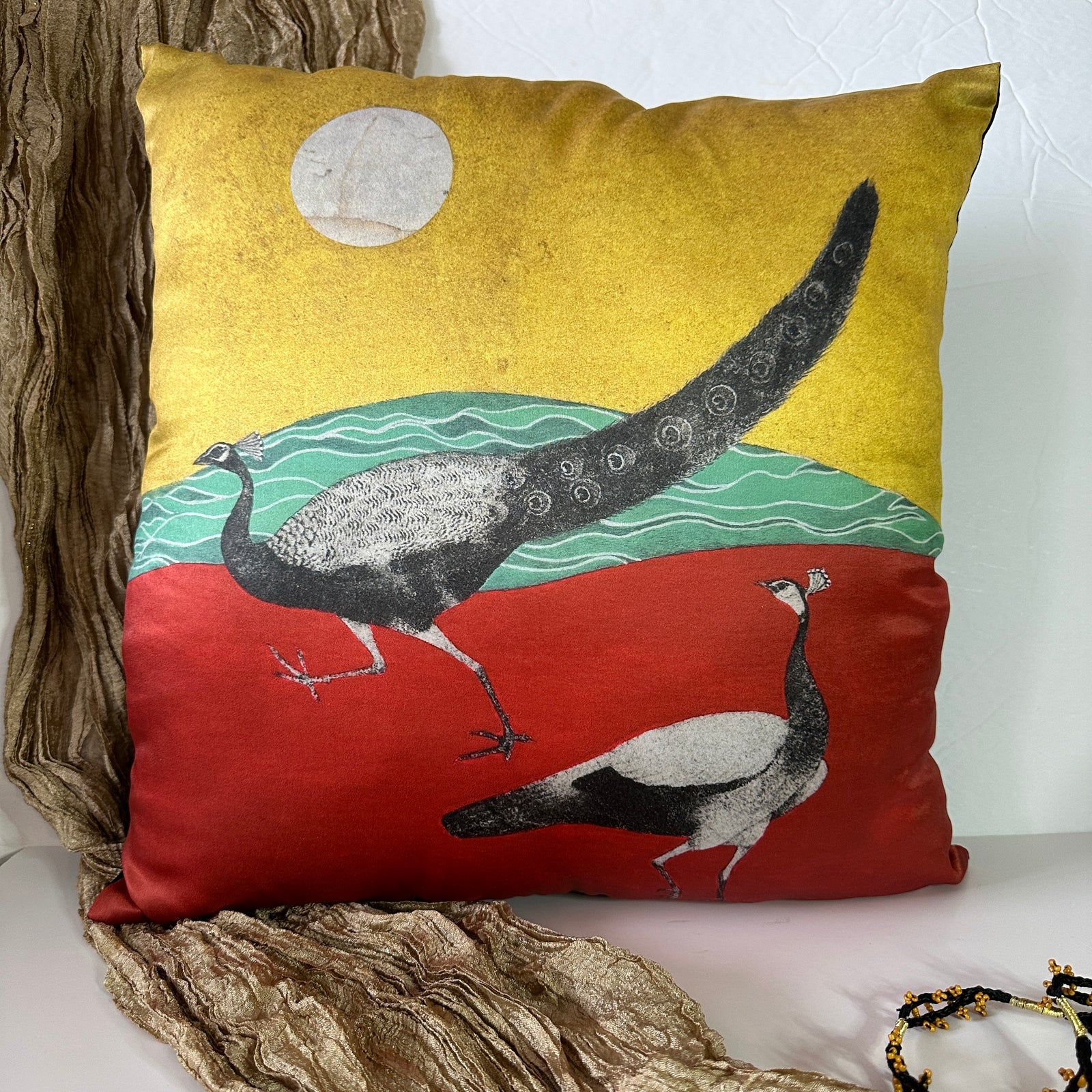 A vibrant Mughal miniature art cushion cover featuring a black and white peacock and peahen print on a striking red, green, and gold background.