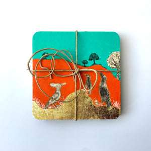 Front view of a hand-painted coasters set tied with string, featuring gold leaf hills and birds on a vibrant orange and turquoise background.