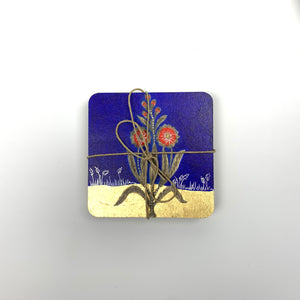  A close-up of a blue botanical hand-painted coaster with red flowers and gold-leaf details, tied with rustic twine.