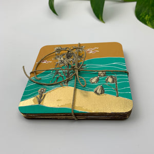 A stack of four hand-painted coasters bound with rustic twine, revealing the plywood layers and gold leaf detailing along the edges.