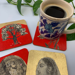 A blue and white ceramic mug sitting on a hand-painted floral coaster, with the other three coasters featuring a Raja, a Rani, and a tree motif laid out on a surface.