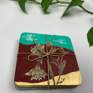 A stack of hand-painted coasters tied with a rustic twine string, highlighting the layered plywood and gold leaf detailing.