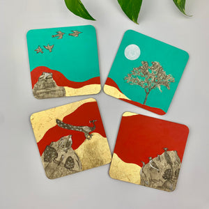 Four handmade drink coasters scattered to display various landscape moments including a full moon, a golden tree, and birds in flight using fine brushwork.