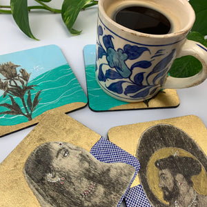 A blue floral ceramic mug is placed on one botanical-themed hand painted coaster, while the other pieces are staggered around it, displaying the portrait of a Mughal woman, a Mughal man and the vibrant gold leaf art.