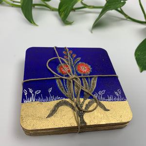 A complete set of hand-painted coasters tied together with twine, showing the deep blue floral design on top and the thick plywood edges of the stack.
