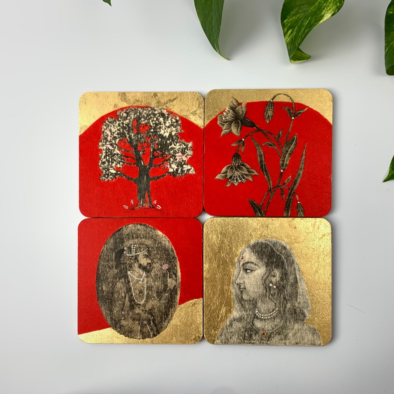 A set of four hand-painted coasters featuring Mughal miniature art, including a Raja, a Rani, and floral motifs on red and gold backgrounds.
