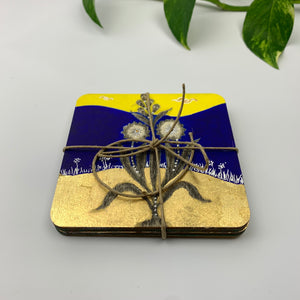 A stack of four hand-painted coasters secured with a jute twine bow, highlighting the thick plywood edges and a blue background botanical motif.